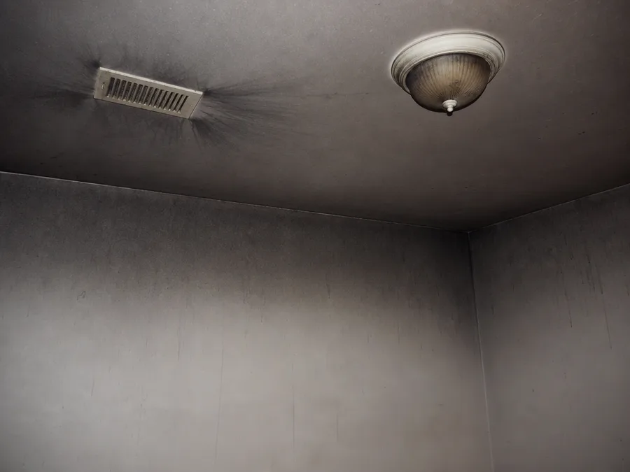 A bedroom ceiling and upper walls coated in grey soot, with black streaks fanning out from an air vent grille